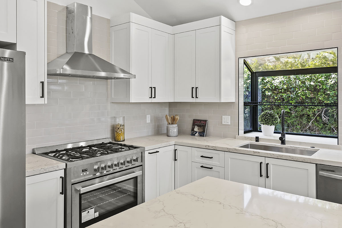 Custom white frameless kitchen cabinets with marble countertops and stainless gas range, built by ATA Custom Cabinets in Los Angeles